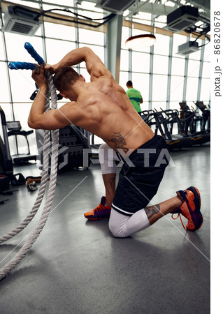 Rear view of Attractive young fit and toned sportswoman working out with battle ropes. Motion blur 86820678