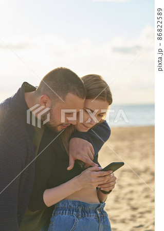 Young couple standing on sandy beach and looking at smartphone, man points finger at mobile Young couple standing on sandy beach and looking at smartphone, man points finger at mobile 86822589