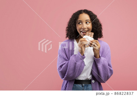 Cheerful millennial African American lady eating chocolate bar over pink studio background, copy space 86822837