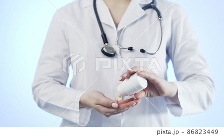 Close-up of an unrecognizable woman, a doctor, holding a jar of pills and throwing it into her hand 86823449