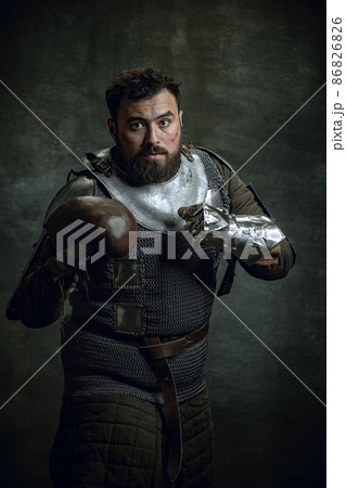Portrait of medieval warrior or knight with dirty wounded face boxing gloves isolated over dark background. Comparison of eras, history Portrait of medieval warrior or knight with dirty wounded face boxing gloves isolated over dark background. Comparison of eras, history 86826826