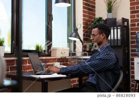 Office startup employee typing on laptop working on market research pie chart Office startup employee typing on laptop working on market research pie chart 86828093