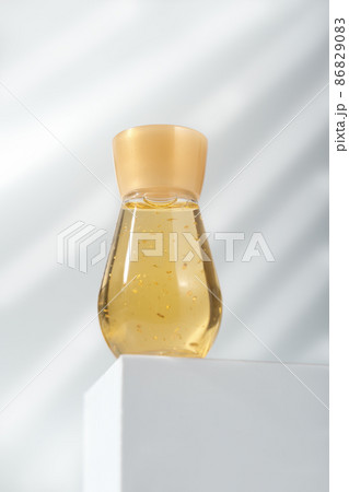 a bottle of cosmetic liquid with golden sparkles on white podium or pedestal. enzyme solution for face skin peeling. beauty care and cosmetology. 86829083