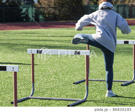 Runner perfoming trail leg hurdle drills on a green turf field Runner perfoming trail leg hurdle drills on a green turf field 86830285