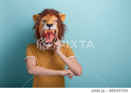 Young woman in lion mask with hand on chin, thinking, pensive expression, isolated on blue   86830700