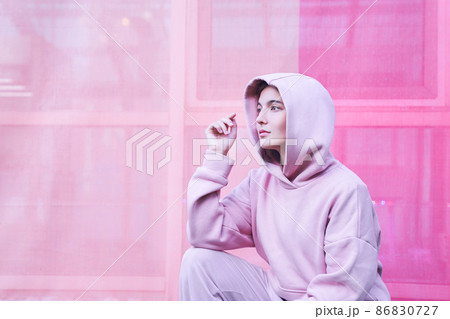 A young woman on an isolated pink background. She sits with one hand on her knee and looks away with a thoughtful face. High quality photo A young woman on an isolated pink background. She sits with one hand on her knee and looks away with a thoughtful face. High quality photo 86830727