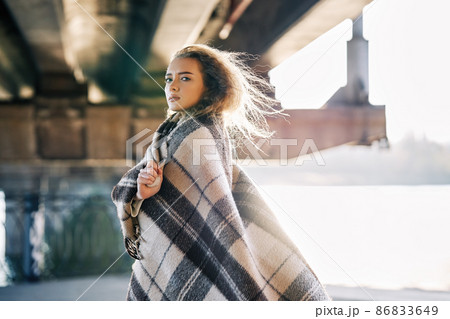 Portrait of pretty confident woman wrapped in wool blanket looking to camera posing on urban street background with copy space 86833649