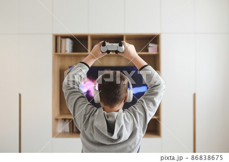 Boy in headphones watching television, teenager boy playing video game in front of screen at home 86838675