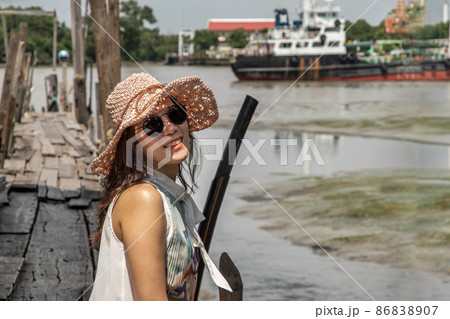 The girl in casual clothes are sitting smiling happily on the old wooden pier by the river. The girl in casual clothes are sitting smiling happily on the old wooden pier by the river. 86838907