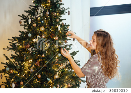 Young woman decorates the Christmas tree with toys. Young woman decorates the Christmas tree with toys. 86839059