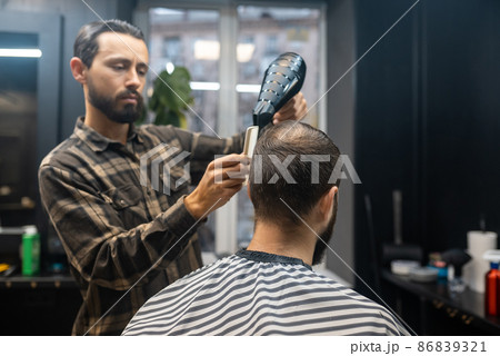 The master in the barbershop is styling the client's hair 86839321