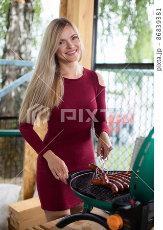 A very shapely girl is standing at the grill turning the sausages inside out. A very shapely girl is standing at the grill turning the sausages inside out. 86839381