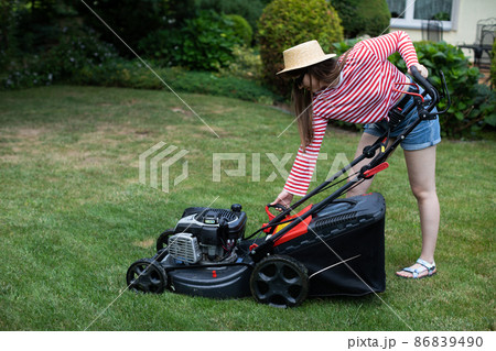 The girl pulls the lever from the manual start of the garden mower. The girl pulls the lever from the manual start of the garden mower. 86839490