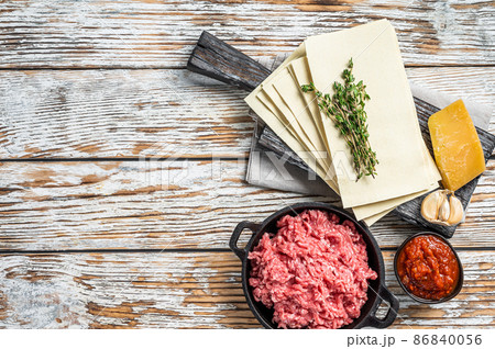 Lasagne raw sheets and other ingredients. White wooden background. Top view. Copy space Lasagne raw sheets and other ingredients. White wooden background. Top view. Copy space 86840056