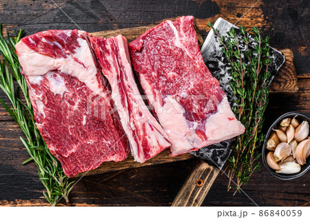 Raw beef calf short ribs meat on a butcher cutting board with cleaver. Dark wooden background. Top view Raw beef calf short ribs meat on a butcher cutting board with cleaver. Dark wooden background. Top view 86840059