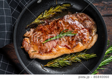 Grilled striploin beef meat steak in a pan with herbs. Dark wooden background. Top view Grilled striploin beef meat steak in a pan with herbs. Dark wooden background. Top view 86840060
