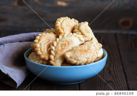 Freshly fried hand pies with meat in a bowl on a wooden background. Close up. 86840109