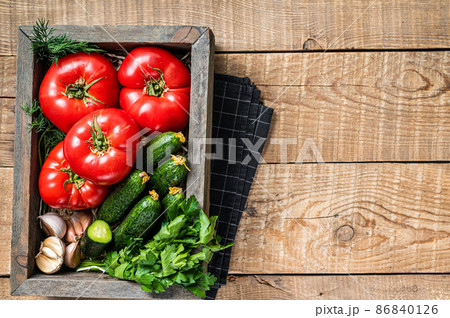 Fresh vegetables in a wooden box, red tomatoes, green cucumbers with herbs. Wooden background. Top view. Copy space Fresh vegetables in a wooden box, red tomatoes, green cucumbers with herbs. Wooden background. Top view. Copy space 86840126