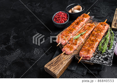 Uncooked Raw Adana shish kebab on butcher board with rosemary. Black background. top view. Copy space 86840553