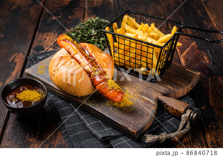 Currywurst Bratwurst sausage in a bun with curry sauce and French fries. Wooden background. Top view 86840718