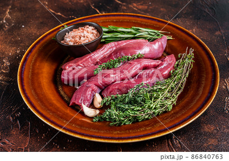 Uncooked Raw lamb tenderloin Fillet Meat in rustic plate with thyme and rosemary. Dark background. Top view Uncooked Raw lamb tenderloin Fillet Meat in rustic plate with thyme and rosemary. Dark background. Top view 86840763