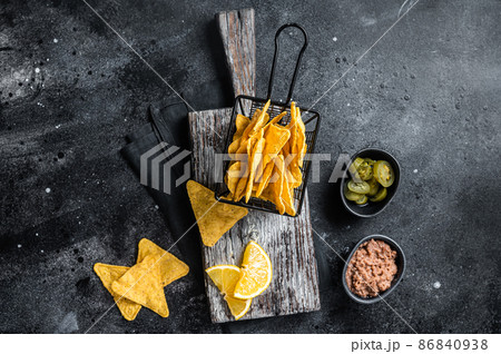 Mexican nachos corn chips with Chili con carne and jalapeno in a basket. Black background. Top view Mexican nachos corn chips with Chili con carne and jalapeno in a basket. Black background. Top view 86840938