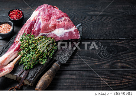 Uncooked Raw lamb mutton leg with herbs on butcher cutting board. Black wooden background. Top view. Copy space Uncooked Raw lamb mutton leg with herbs on butcher cutting board. Black wooden background. Top view. Copy space 86840983