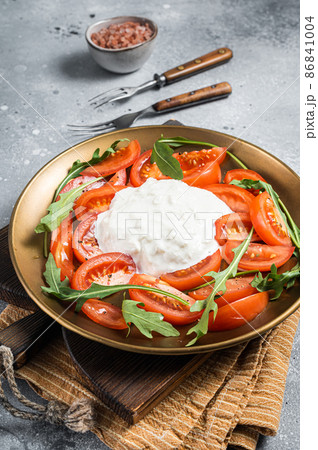 Italian cheese stracciatella burrata on plate with fresh tomatoes and arugula. Gray background. Top view 86841004