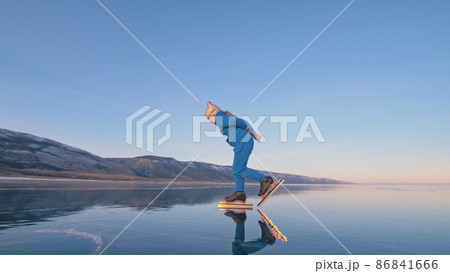 The child train on ice professional speed skating. The girl skates in the winter in sportswear, sport glasses, suit. Outdoor slow motion. 86841666
