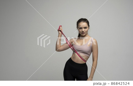 Weight loss and diet concepts. Attractive gorgeous sporty woman in sportswear outfit holding a pink measuring tape around her thighs on white background. Weight loss and diet concepts. Attractive gorgeous sporty woman in sportswear outfit holding a pink measuring tape around her thighs on white background. 86842524