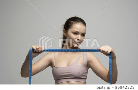 Sexy attractive brunette female in sportswear outfit holding a blue measuring tape in front of her face. Weight loss and diet concepts. Health care and healthy nutrition. Perfect slim body. Sexy attractive brunette female in sportswear outfit holding a blue measuring tape in front of her face. Weight loss and diet concepts. Health care and healthy nutrition. Perfect slim body. 86842525