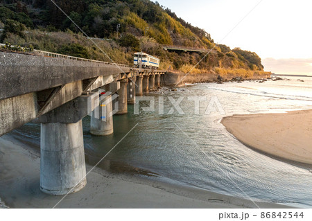 日向の南部の太平洋に昇るオレンジ色の朝日をうけて岩場の海岸線を走る日南線白いキハ40 日向の南部の太平洋に昇るオレンジ色の朝日をうけて岩場の海岸線を走る日南線白いキハ40 86842544