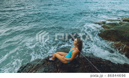 Woman walk near a rock reef hill in stormy morning rain cloudy sea. Concept resort outdoor relax, vacation, loneliness 86844696