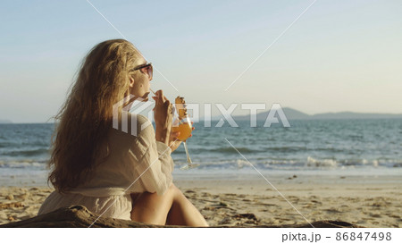 Woman sitting in white dress drinks pineapple cocktail Pina Cola Woman sitting in white dress drinks pineapple cocktail Pina Cola 86847498