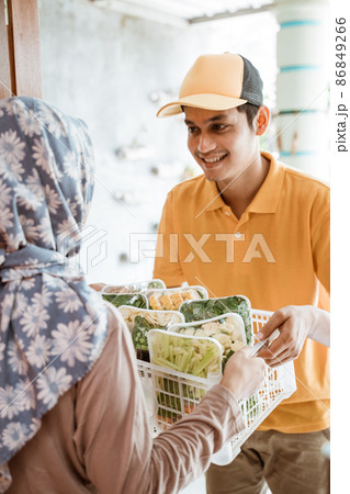 Deliveryman gives vegetable orders to women in headscarves 86849266
