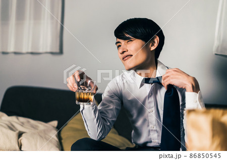 仕事終わりにテイクアウトの食べ物とお酒を飲む若いビジネスマン 仕事終わりにテイクアウトの食べ物とお酒を飲む若いビジネスマン 86850545