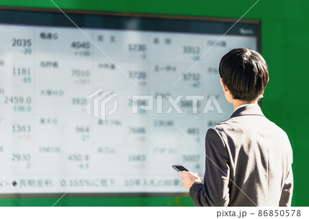 株価ボードを見る男性（スマートフォンを手に持つ） 86850578