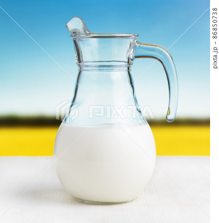 Jug of milk on meadow background. Half full pitcher Jug of milk on meadow background. Half full pitcher 86850738