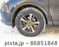 The wheel of a dirty car on a background of snow on a sunny winter morning. 86851848