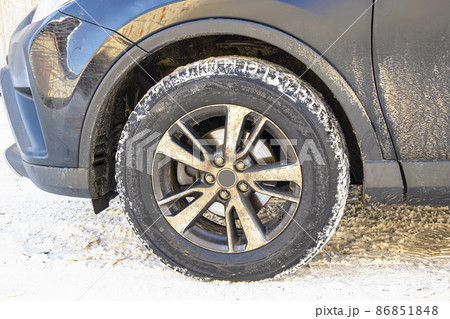 The wheel of a dirty car on a background of snow on a sunny winter morning. 86851848
