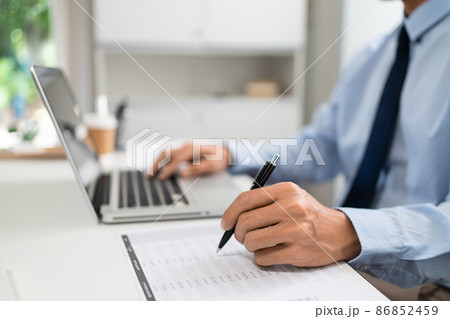 Working Man Conept The male officer sitting in the office, laying his left hand on the laptop, and writing something on the paper with his right hand 86852459