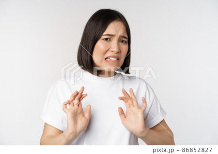 Disgusted asian woman rejecting smth, grimacing from dislike and aversion, stare with cringe, refusing offer, standing over white background 86852827