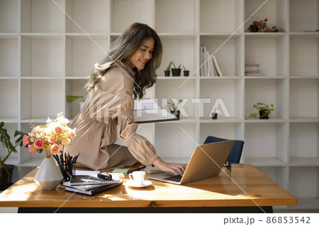 Attractive asian woman sitting on wooden table and using laptop computer. 86853542