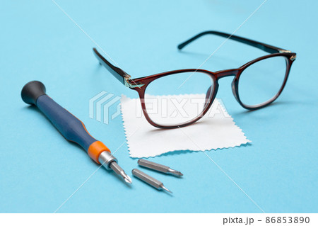 Glasses for vision, a lens cleaning cloth, and a screwdriver for repairs on a blue background. Glasses repair concept. Workshop. Glasses for vision, a lens cleaning cloth, and a screwdriver for repairs on a blue background. Glasses repair concept. Workshop. 86853890