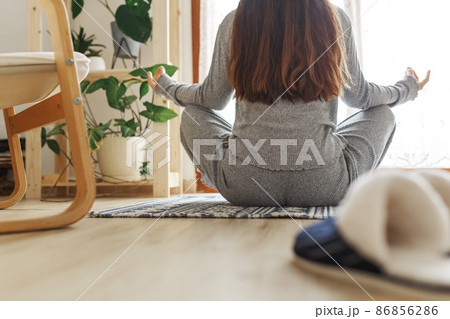 Young female sitting cross-legged in Easy pose, Sukhasana posture and meditating. Practicing yoga at home.Happy young woman enjoying sunny morning meditation routine.  86856286