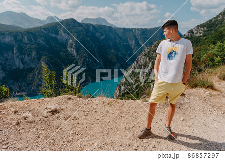 Guy traveler on the background The famous Piva Canyon with its fantastic reservoir. View of road above Piva Lake (Pivsko Jezero) in Montenegro. man looks at river Piva, Montenegro. 86857297