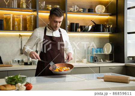 Young chef man tosses steamed vegetables on pan in kitchen Young chef man tosses steamed vegetables on pan in kitchen 86859611