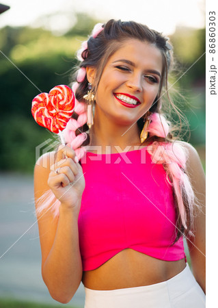 Pretty and positive girl in pink top holding candy 86860303