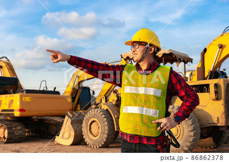 asian technician civil engineer talk with team by walkie talkie and point at inspection survey point for transport construction work project with excavator on engineering site background 86862378