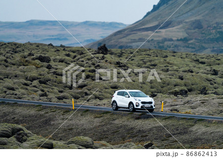 White car driving through vast lava fields covered by moss White car driving through vast lava fields covered by moss 86862413